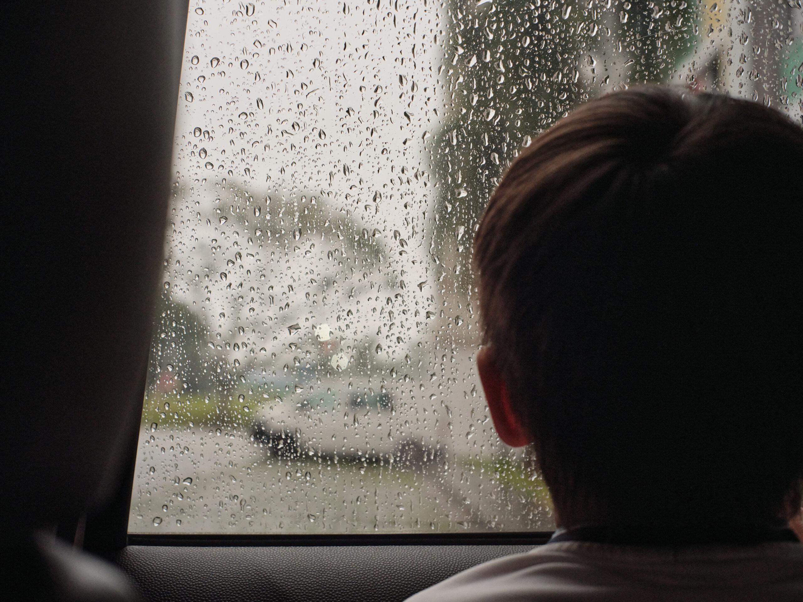 Enfant de dos regardant les gouttes de pluie sur la vitre d'une voiture, ambiance mélancolique